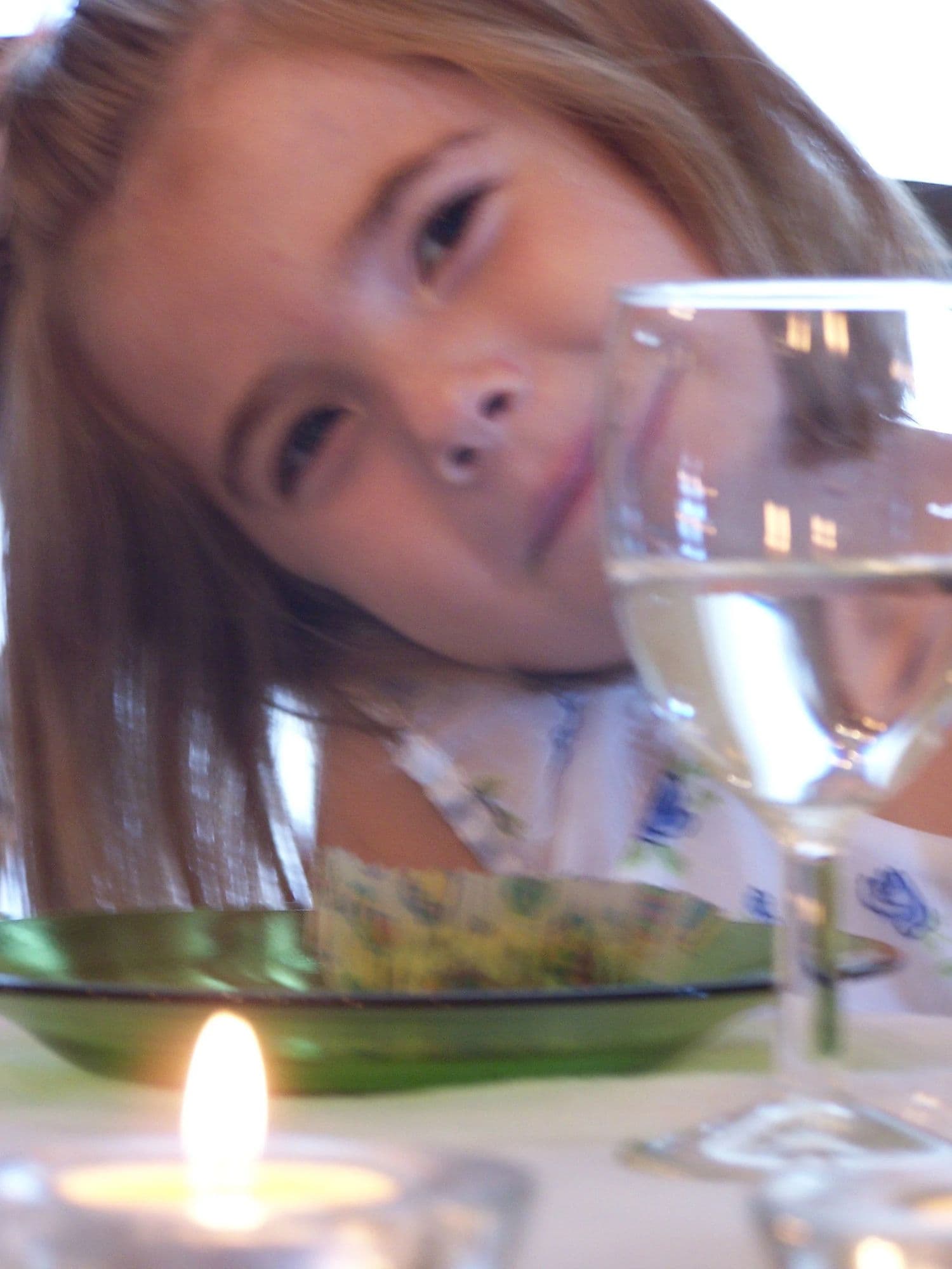 A young girl leaning on a table beside a water glass and a lit candle at a tea party