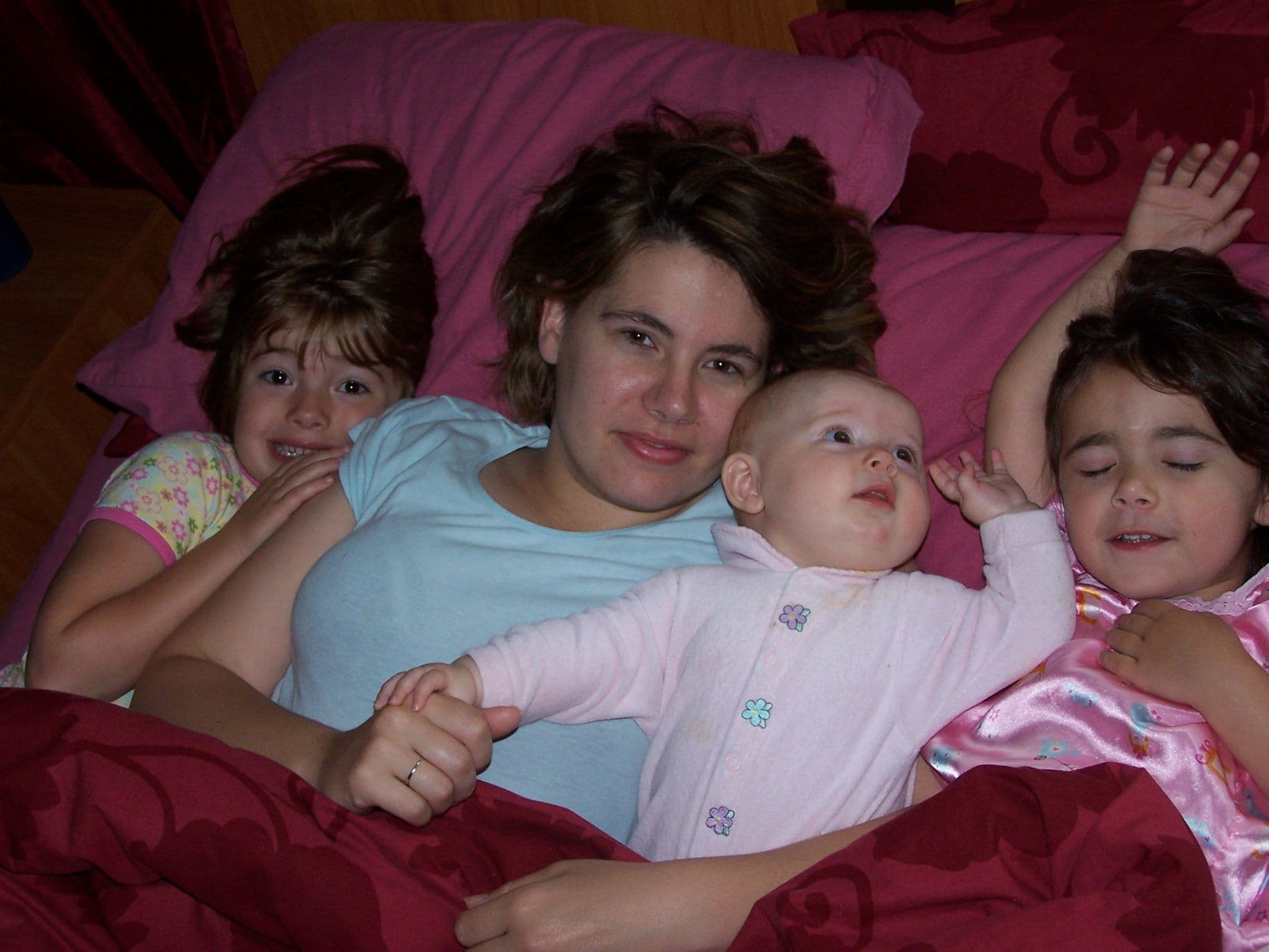 Mother and three girls play in bed