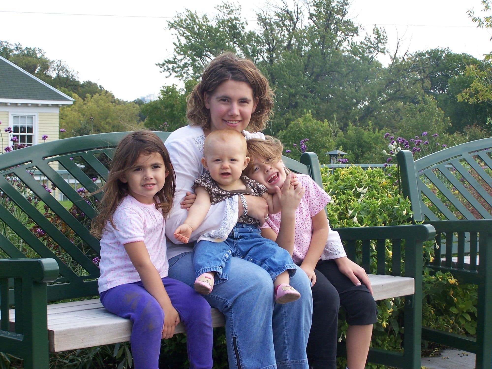 Woman holds three girls on a park bench