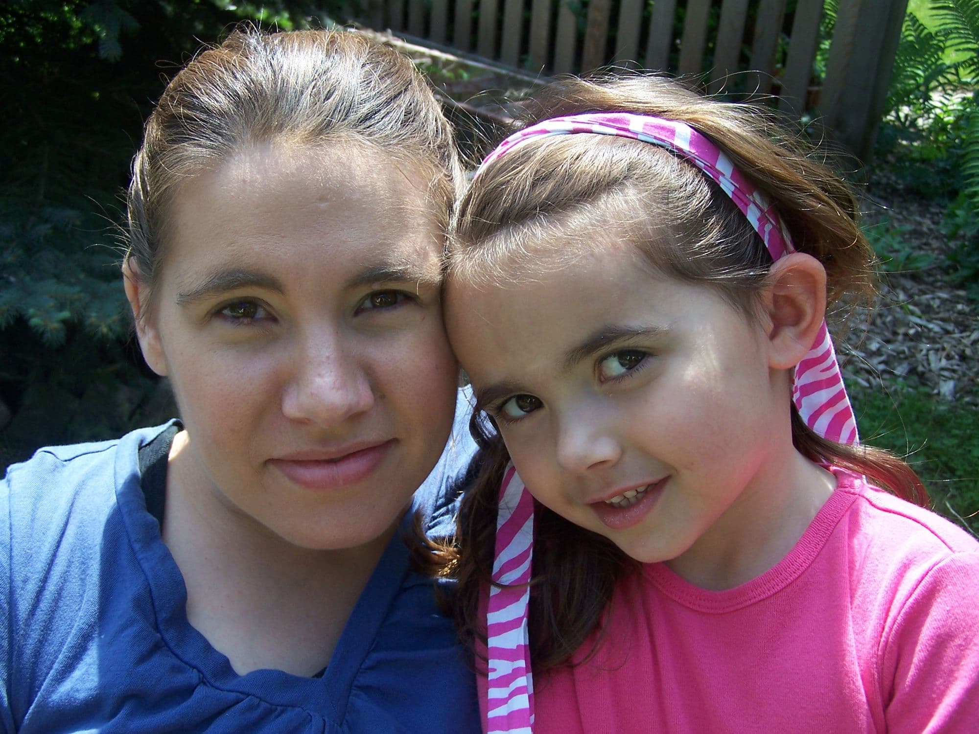 Woman and girl pose cheek to cheek outdoors