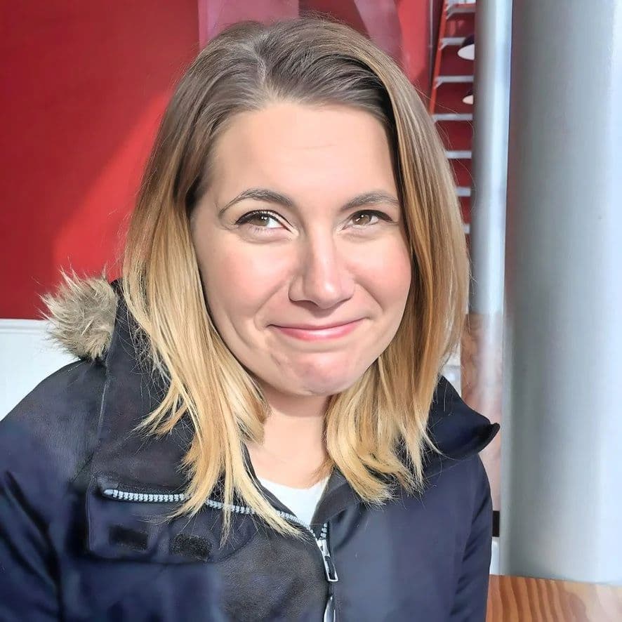 A young woman in a navy winter coat smiling at the camera in front of a red wall
