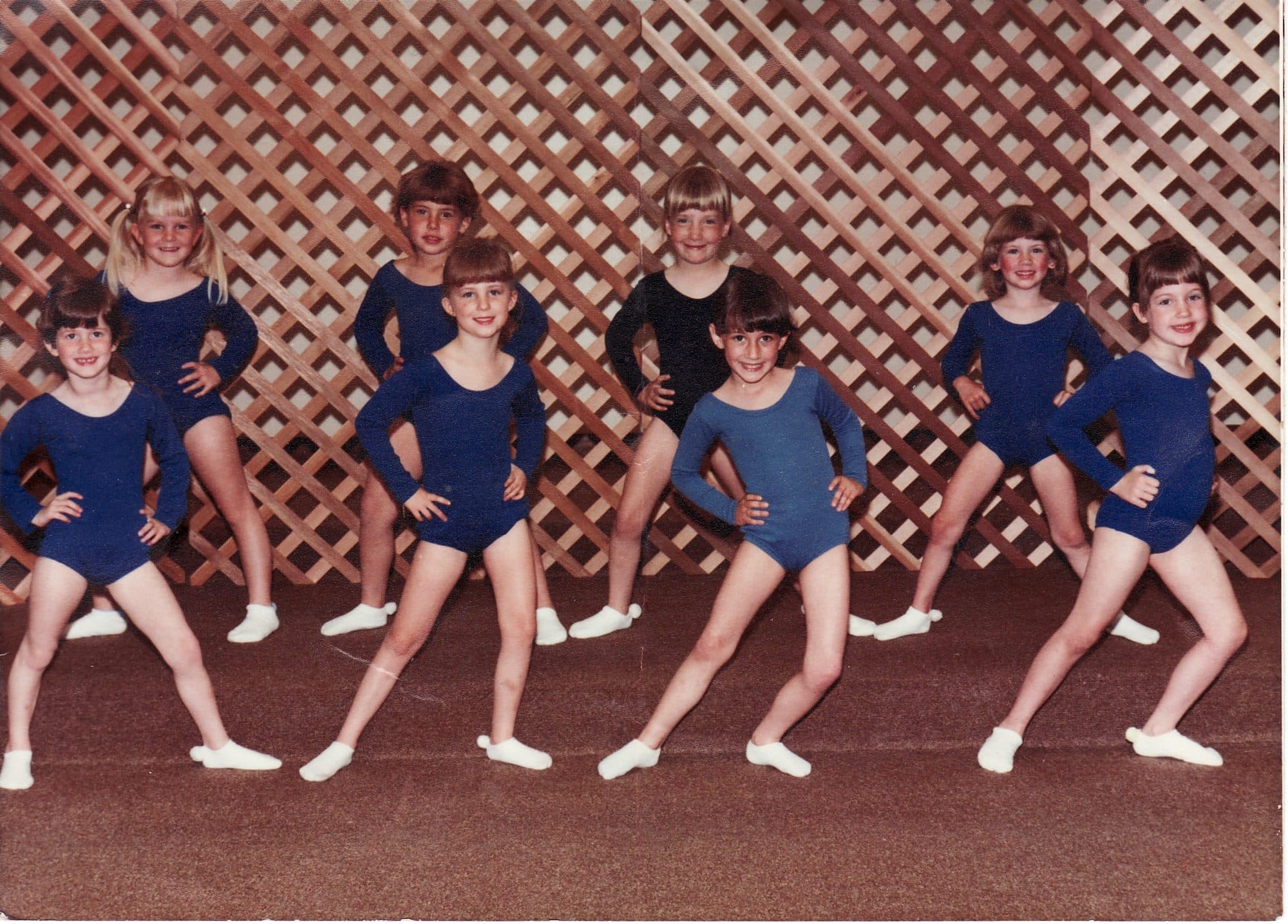 Eight girls posing in matching gymnastics leotards