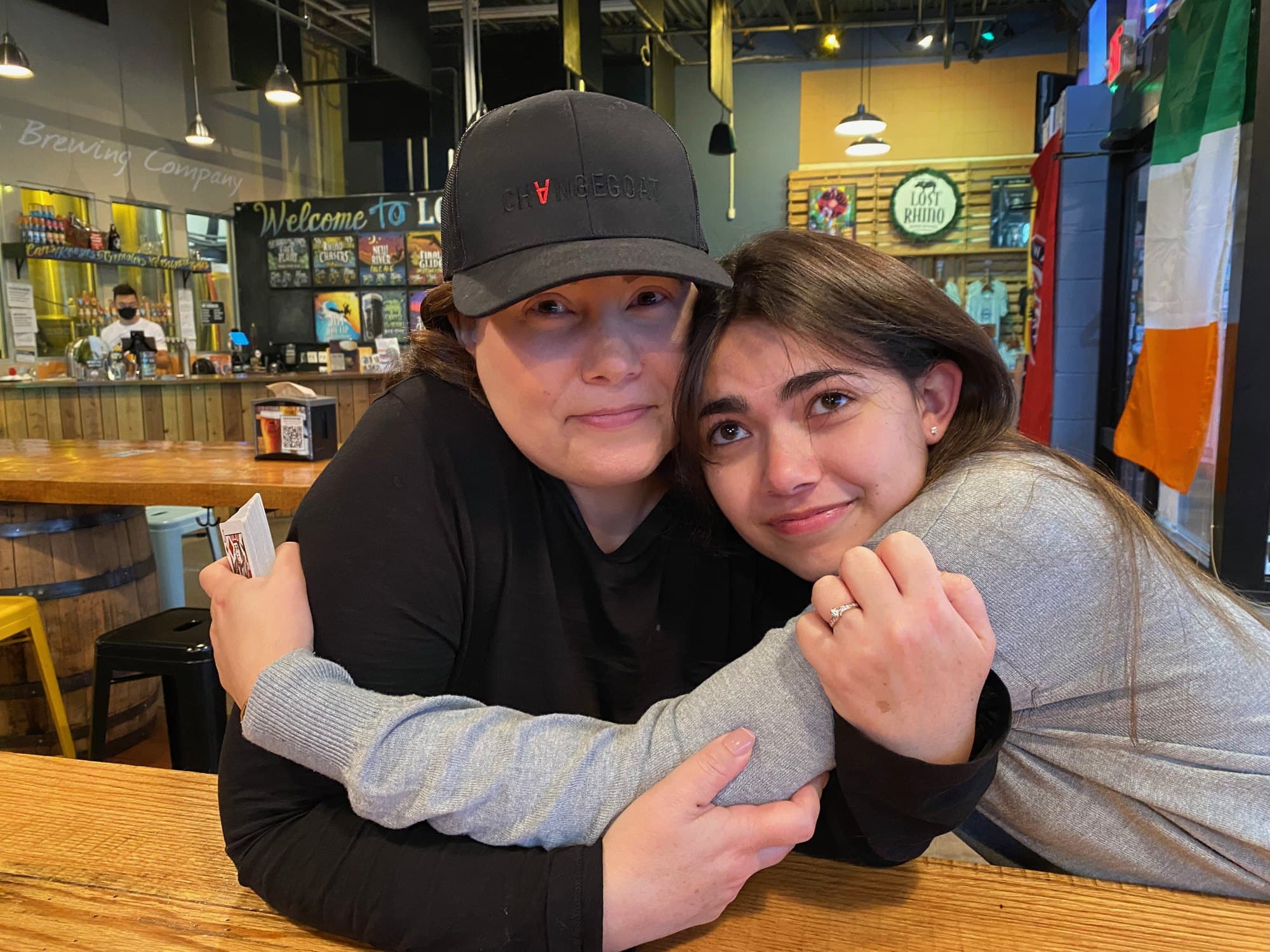 Gretchen and one of her daughters holding on to each other and smiling, in a brewery taproom