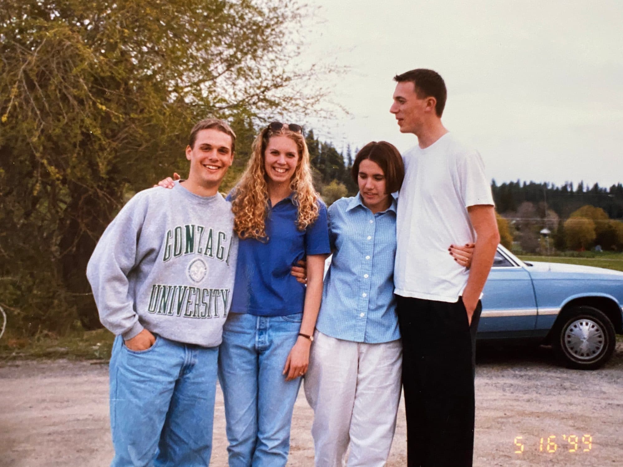 Four college friends posing outdoors by a car