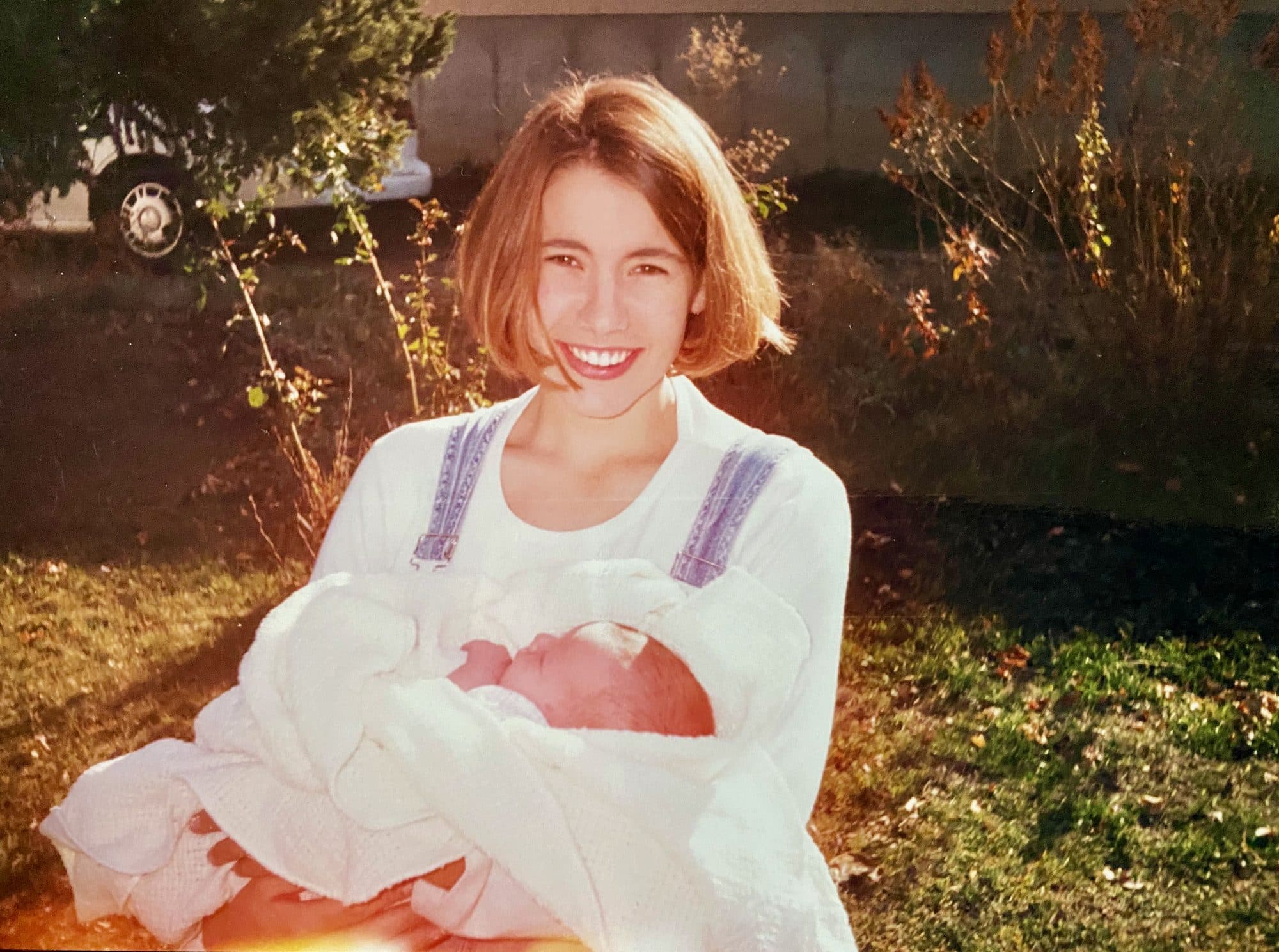 Young woman holding a newborn baby outdoors