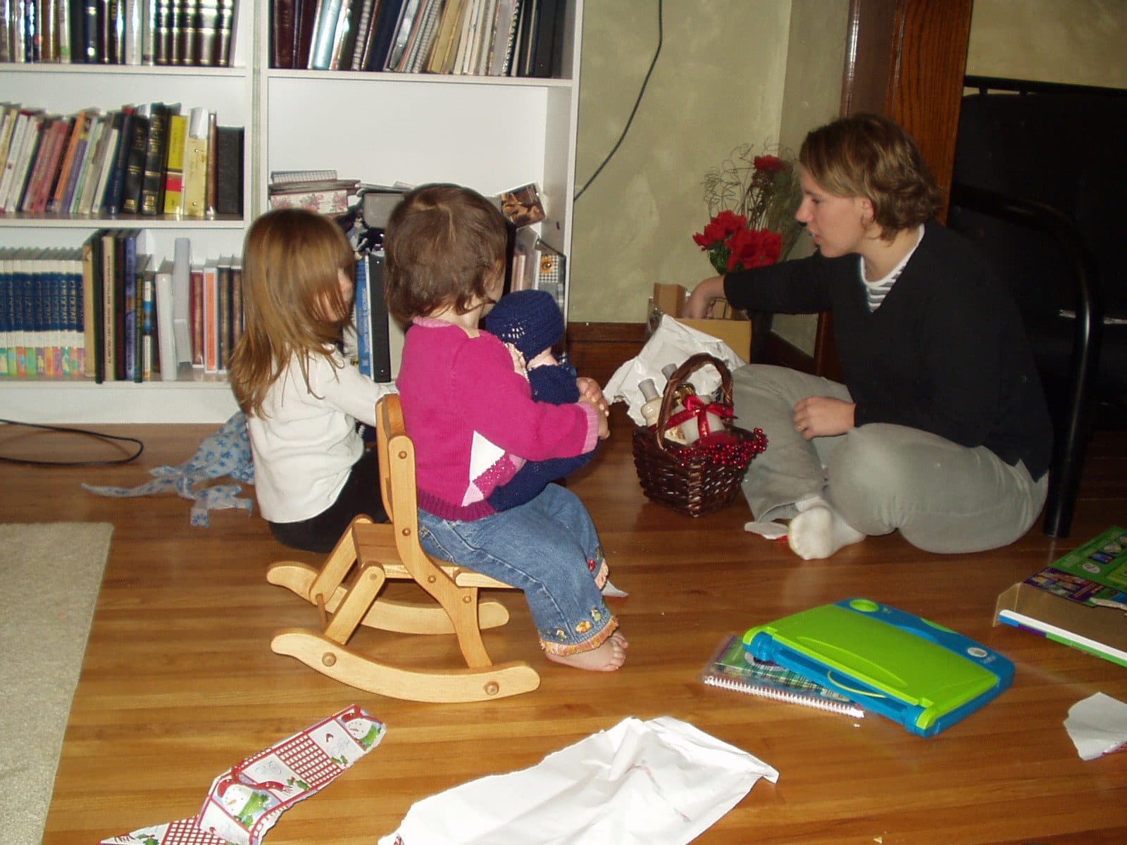 Two girls open gifts near a bookshelf