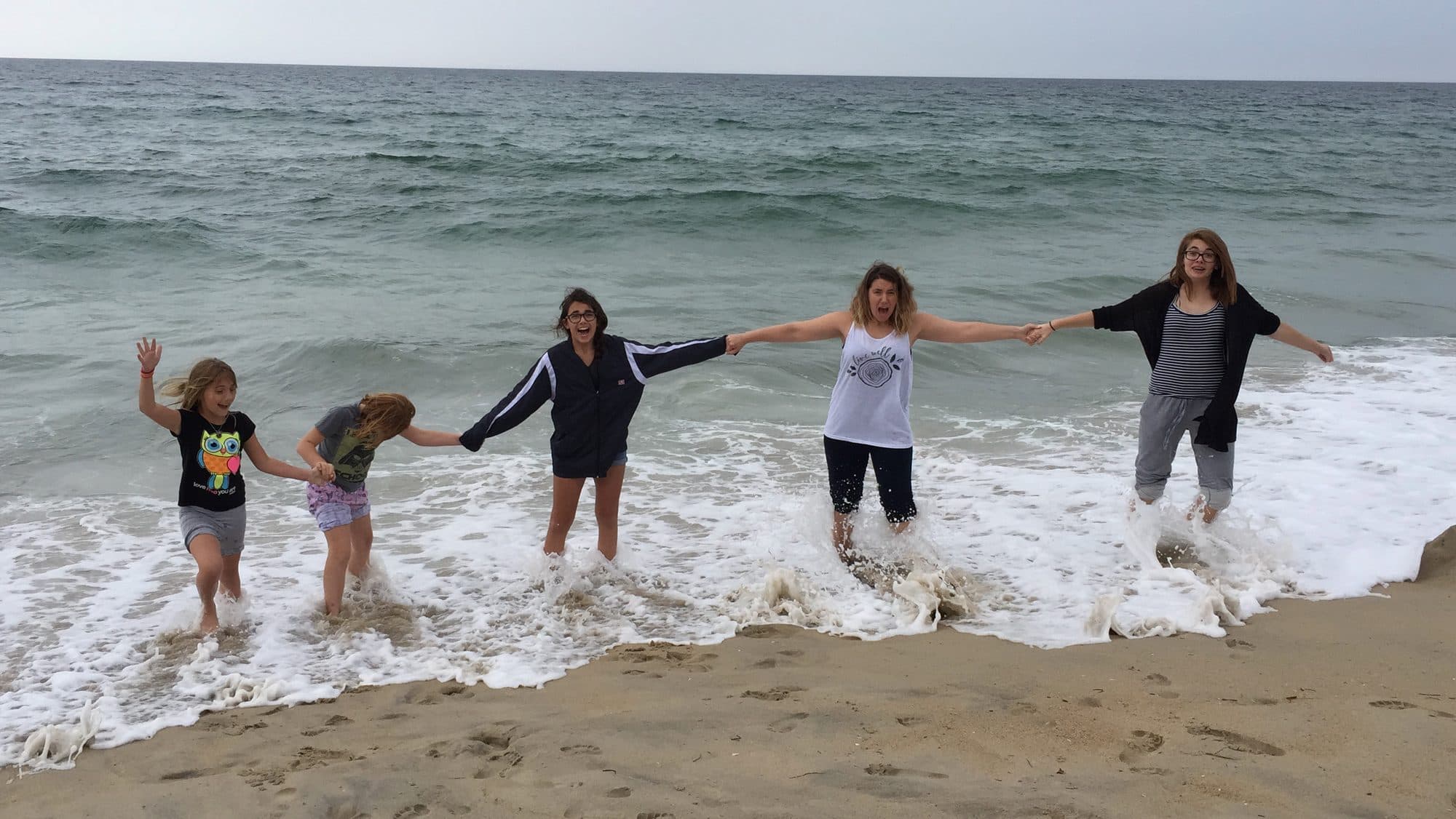 Five people hold hands wading in ocean waves