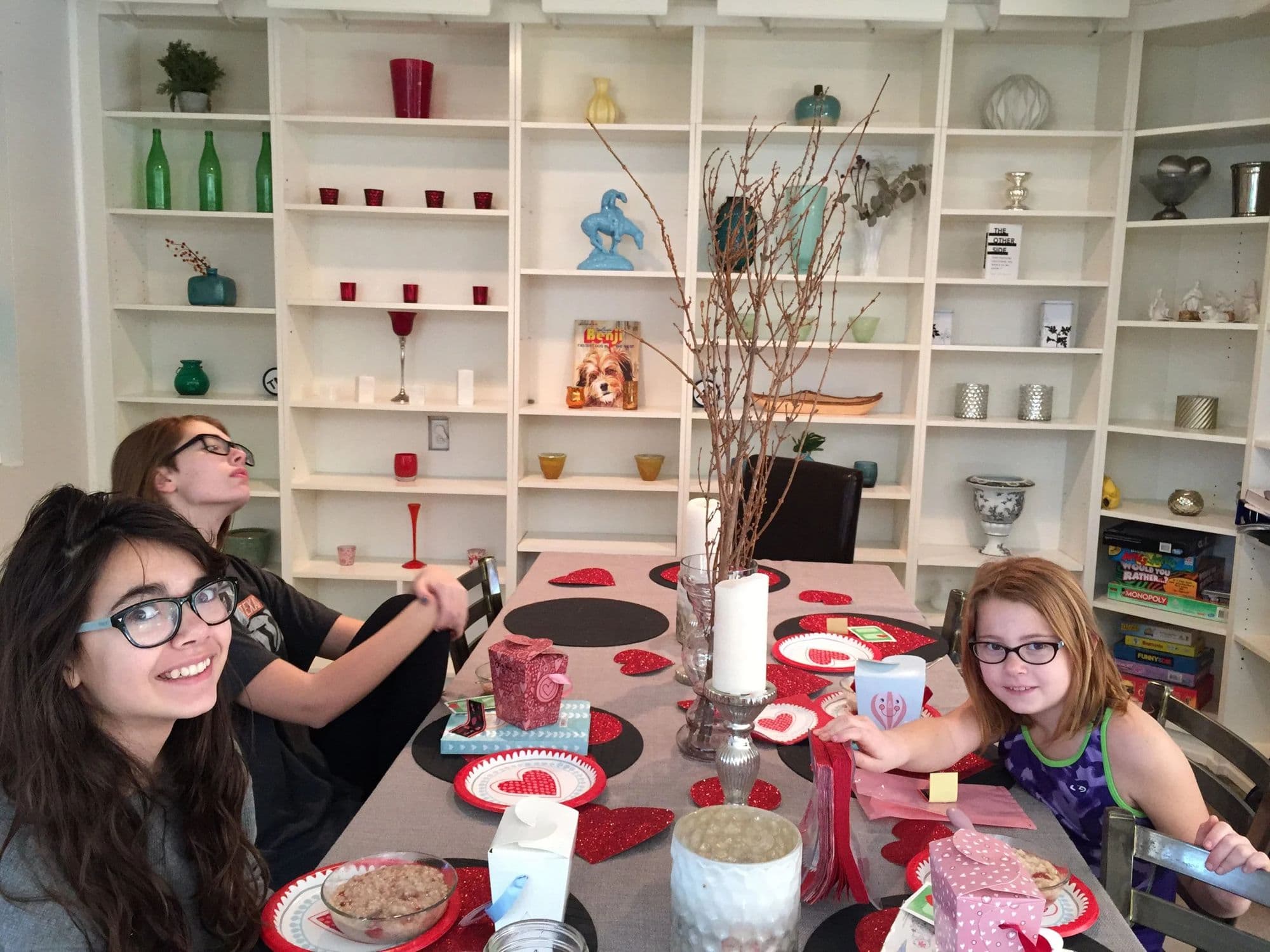 A family Valentine's Day table, the girls seated around it in front of a wall of white shelves