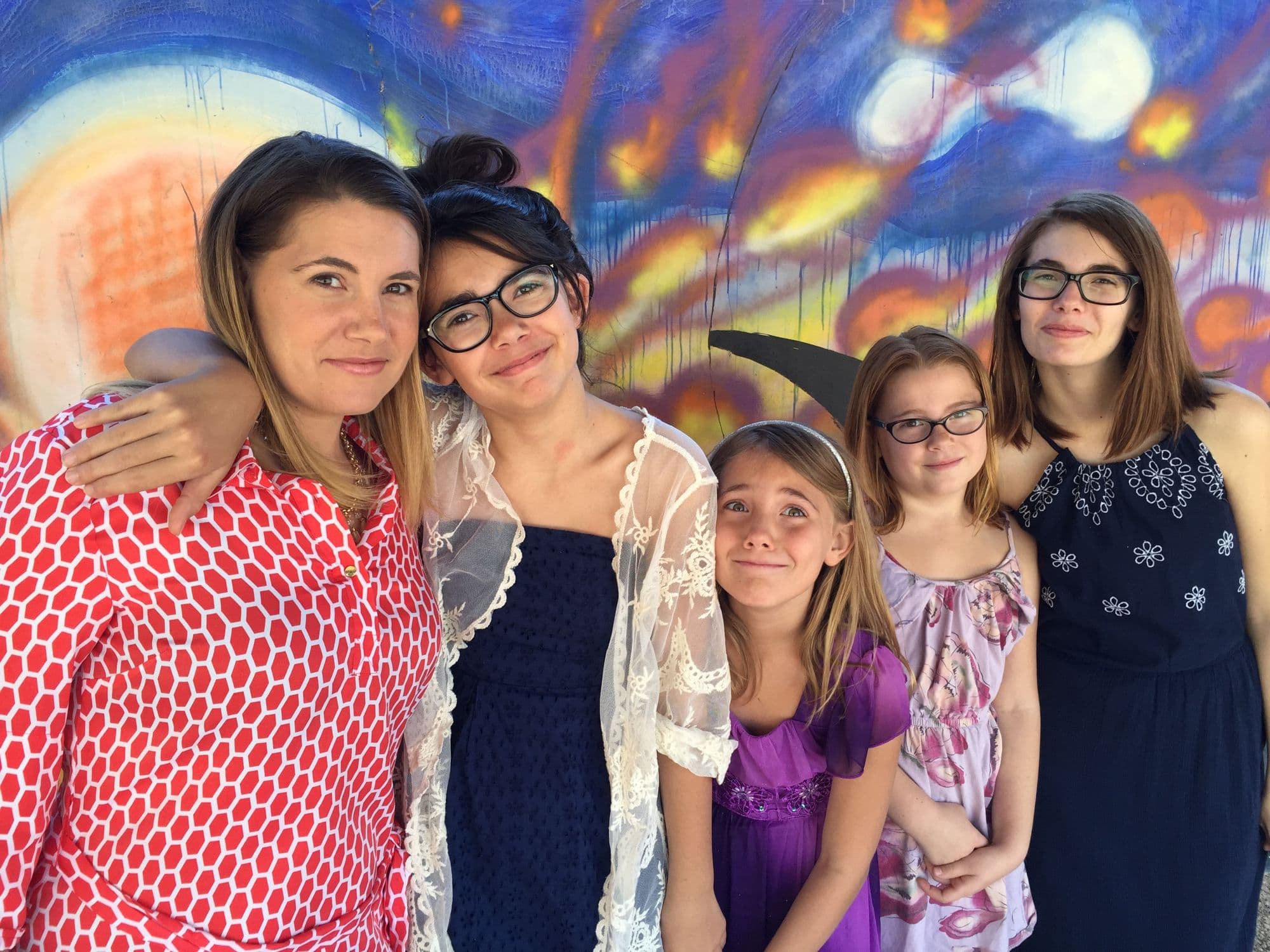 Woman and four girls pose by a colorful mural