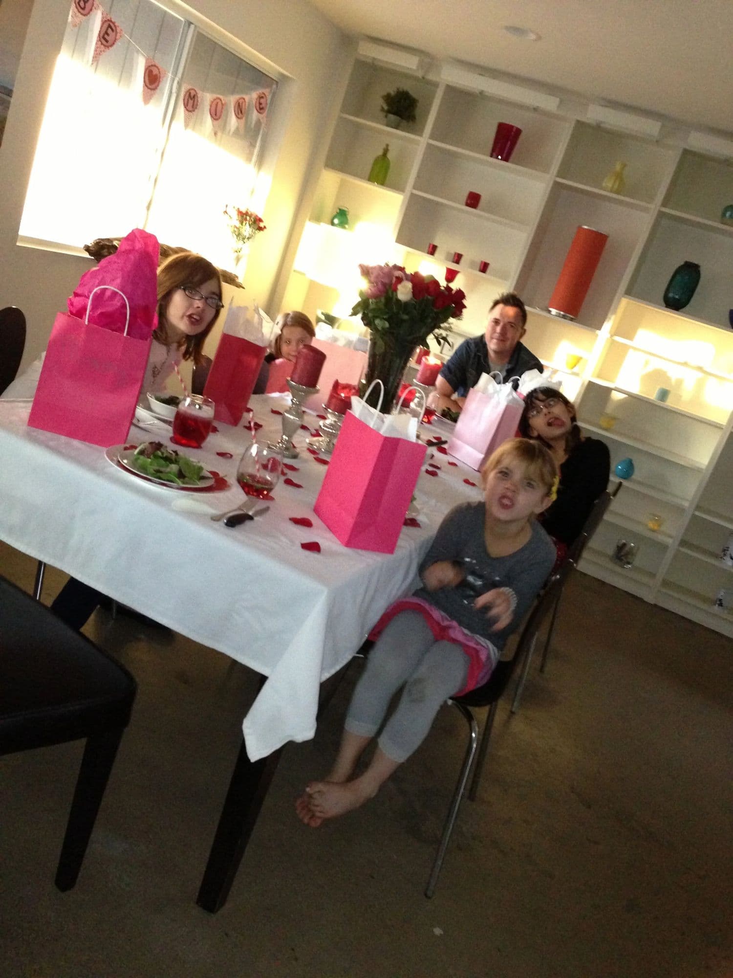 The Valentine's table laid with a white cloth and pink gift bags, the family seated along it