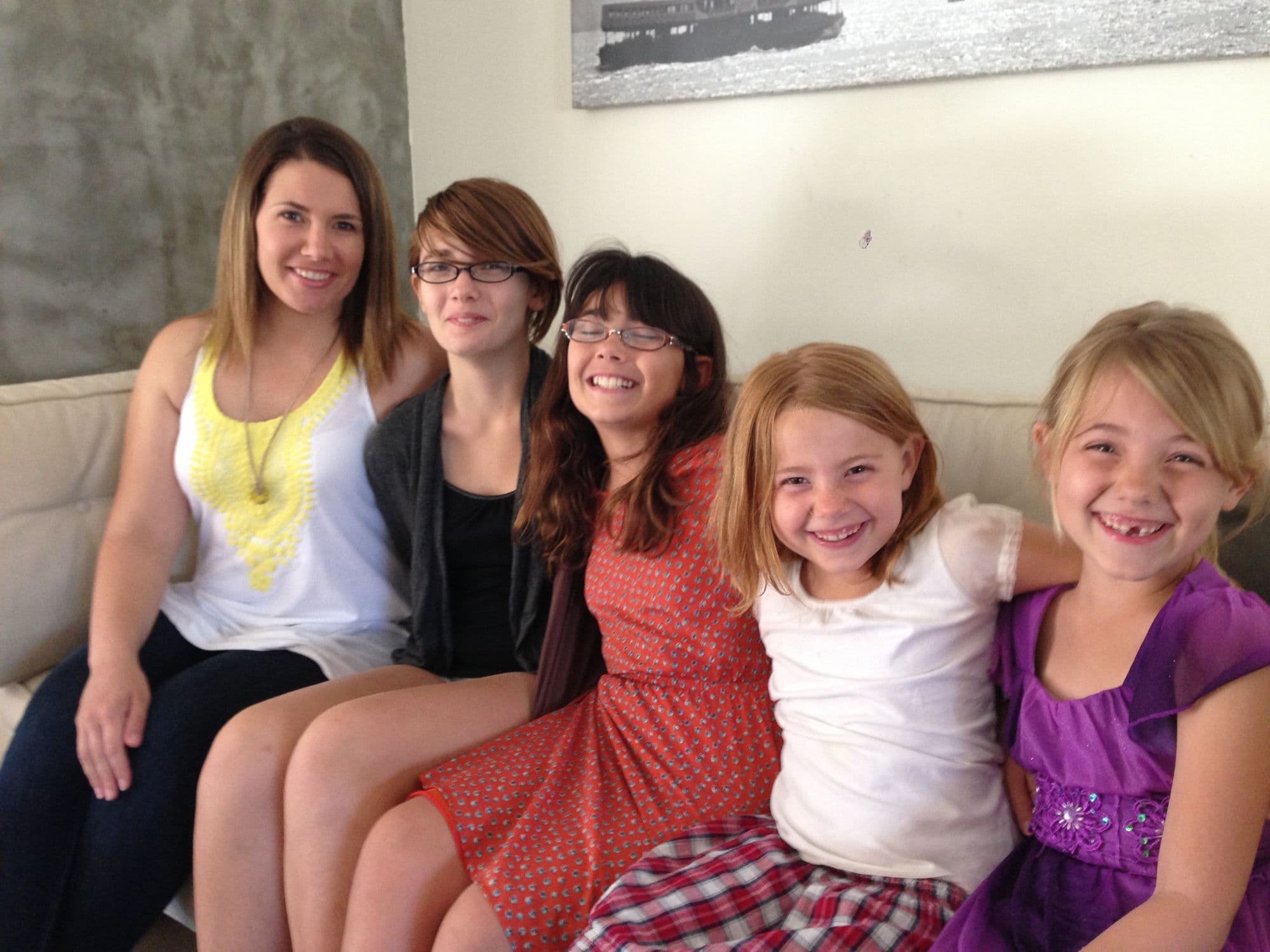 Woman and four girls smile on a couch