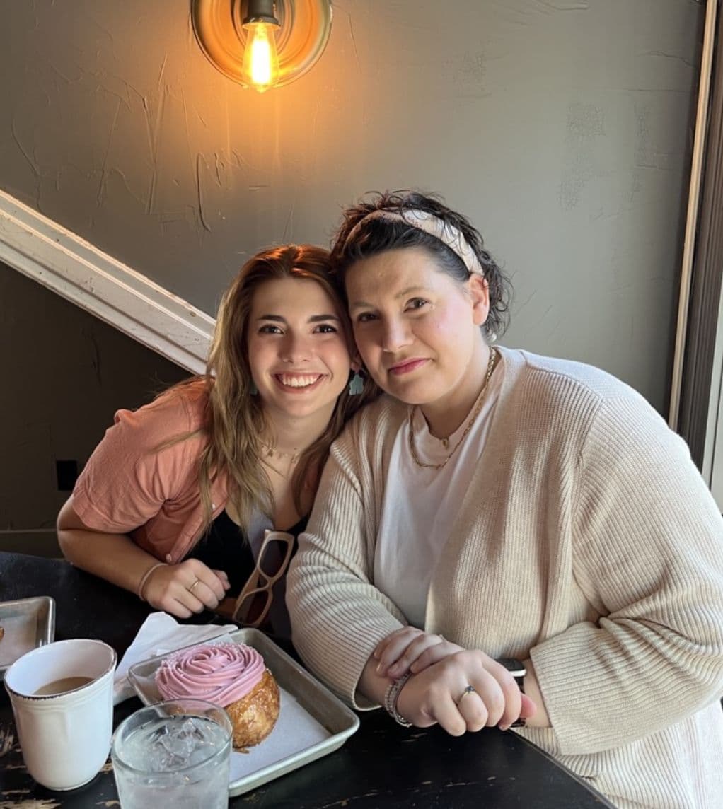 Gretchen in a headscarf and one of her daughters side by side at a café table