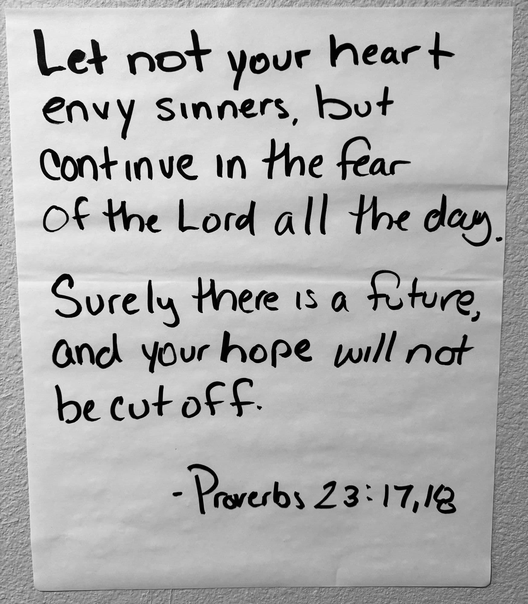 A handwritten sheet of Proverbs 23:17–18 taped to a wall